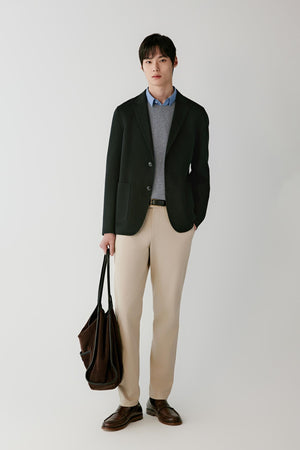 Front view of a man wearing a deep black wool blazer, showing the straight silhouette, notched lapels and patch pockets.