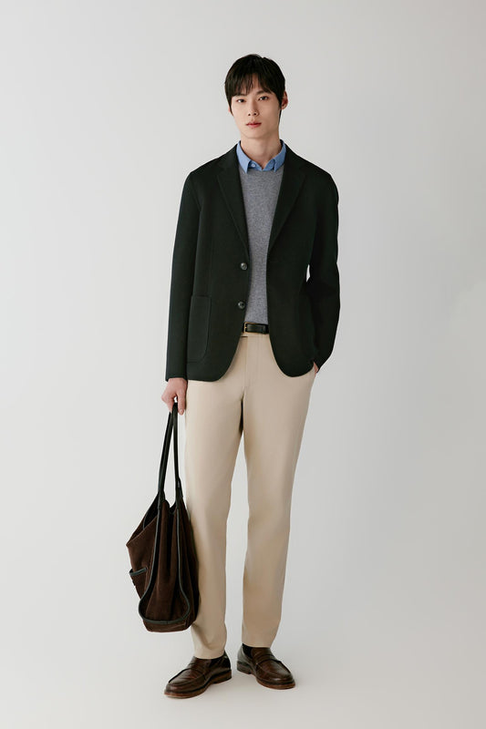 Front view of a man wearing a deep black wool blazer, showing the straight silhouette, notched lapels and patch pockets.