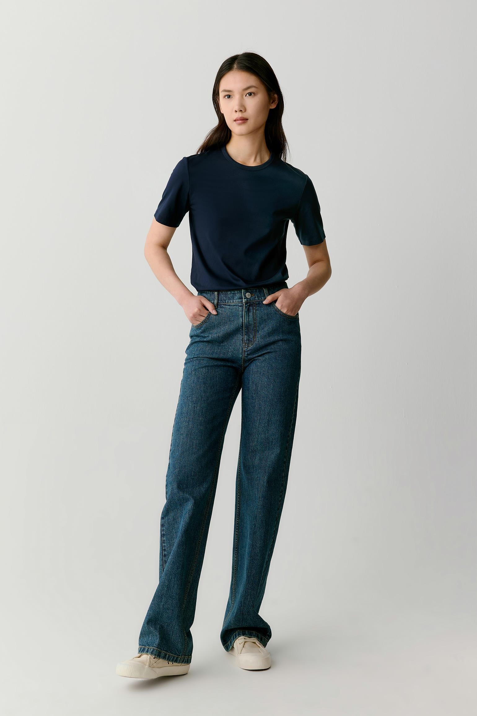 Full-length front view of a navy cotton jersey T-shirt worn with blue denim jeans, showing a straight cut, short sleeves, and a relaxed, natural fit on the body.