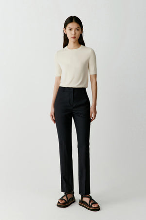 Full-length front view of a model wearing an ivory short-sleeved tee knitted from superfine wool. The tee has a straight relaxed silhouette with a classic round neckline and short sleeves extending halfway down the upper arm. The fine knit creates a lightweight and fluid drape across the torso.