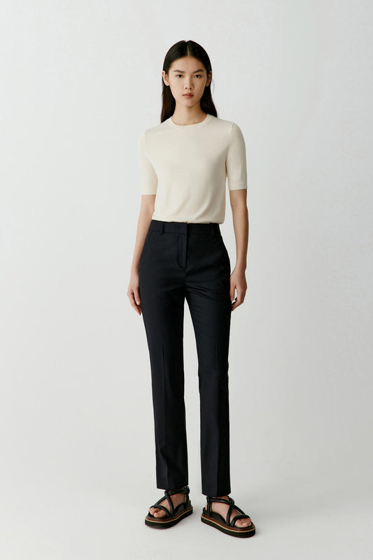 Front view of a woman wearing deep black worsted wool trousers, showing the straight, slightly tapered leg and mid-rise waist.