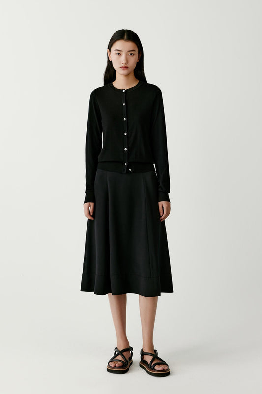 Front view of a woman wearing a deep black wool cardigan, showing the straight silhouette, round neckline and button-front fastening.