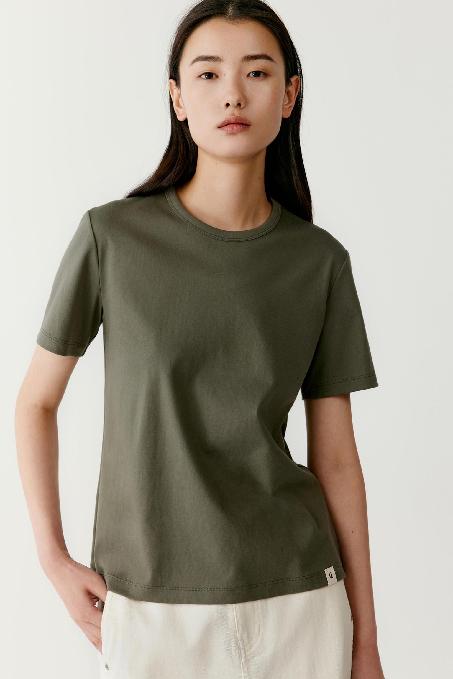 Three-quarter view showing the relaxed proportions and fluid drape of the T-shirt. The image emphasizes the soft hand of the cotton jersey, the smooth surface and the way the fabric follows the body with gentle movement. The dark grey shade reveals subtle tonal depth across the garment.