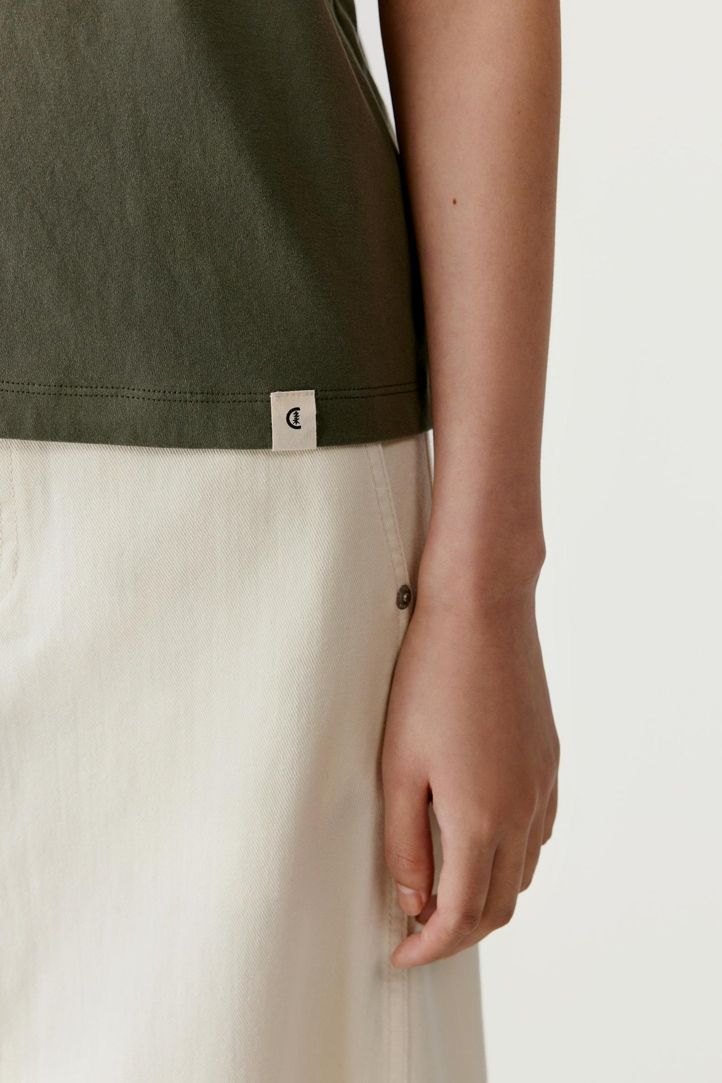 Close-up view of the sleeve and side hem area. The image showcases the lightweight cotton jersey construction, soft drape and clean finishing details, highlighting the fluid quality of the fabric and the understated character of the garment.
