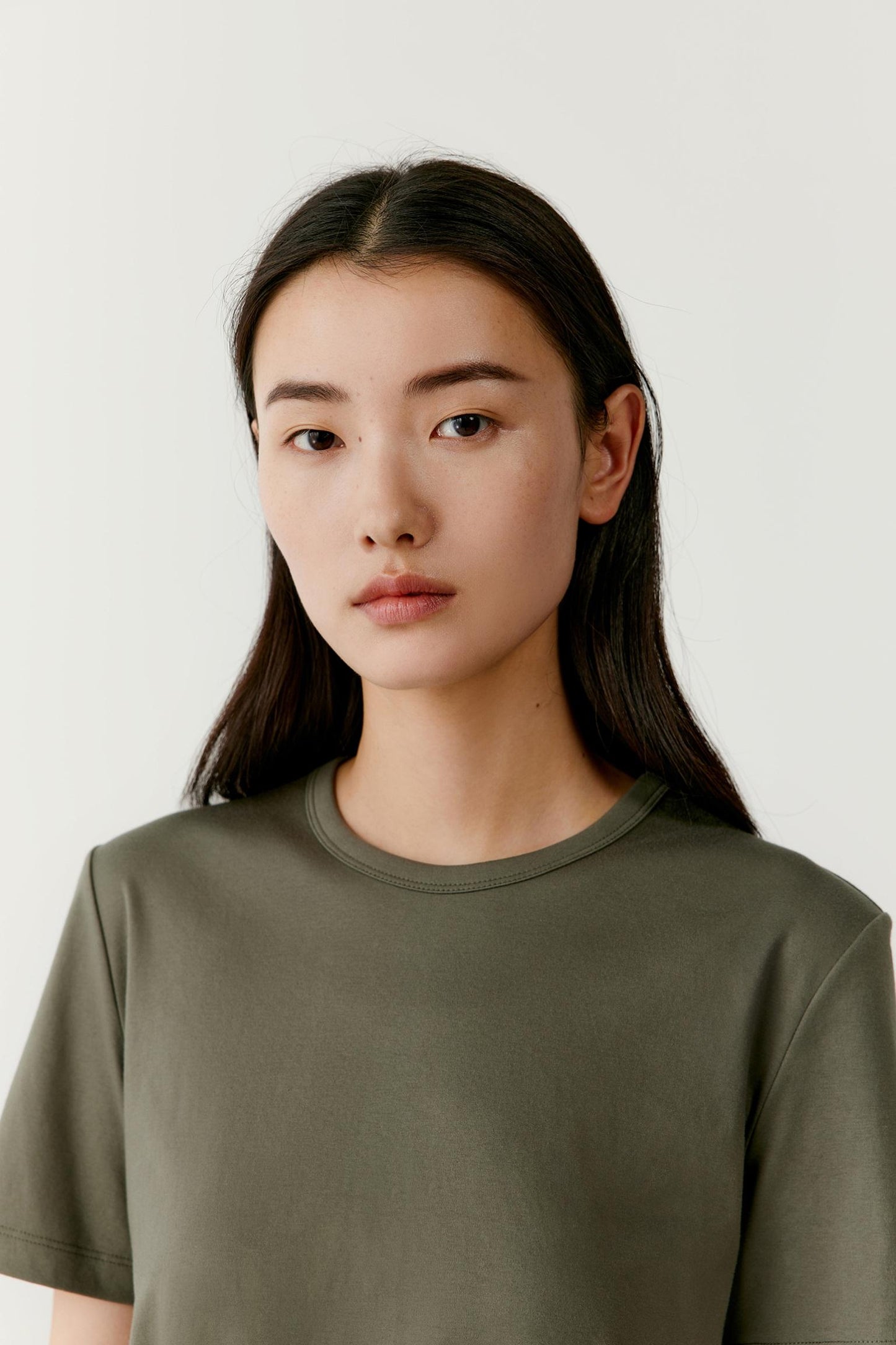 Close-up portrait focusing on the round neckline, shoulder line and upper body construction. The image reveals the smooth jersey surface, clean finishing and subtle texture of the cotton fabric while highlighting the relaxed fit around the neckline.