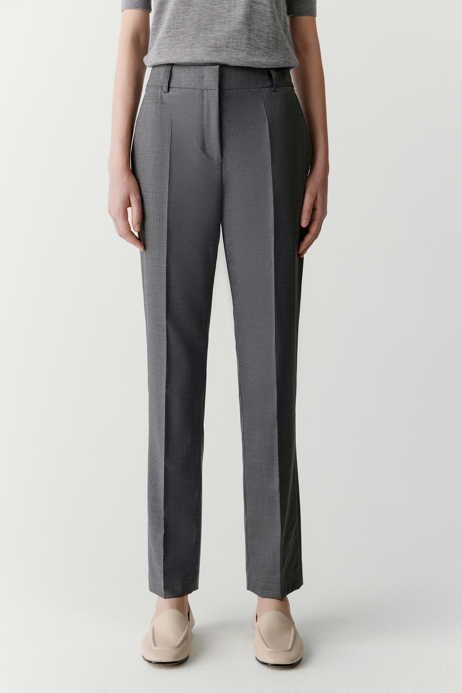 Full-length view focused on the trousers, showing the tapered cut from hip to ankle, the smooth surface of the worsted wool and the precise construction of the leg. The fabric falls cleanly while maintaining subtle structure.