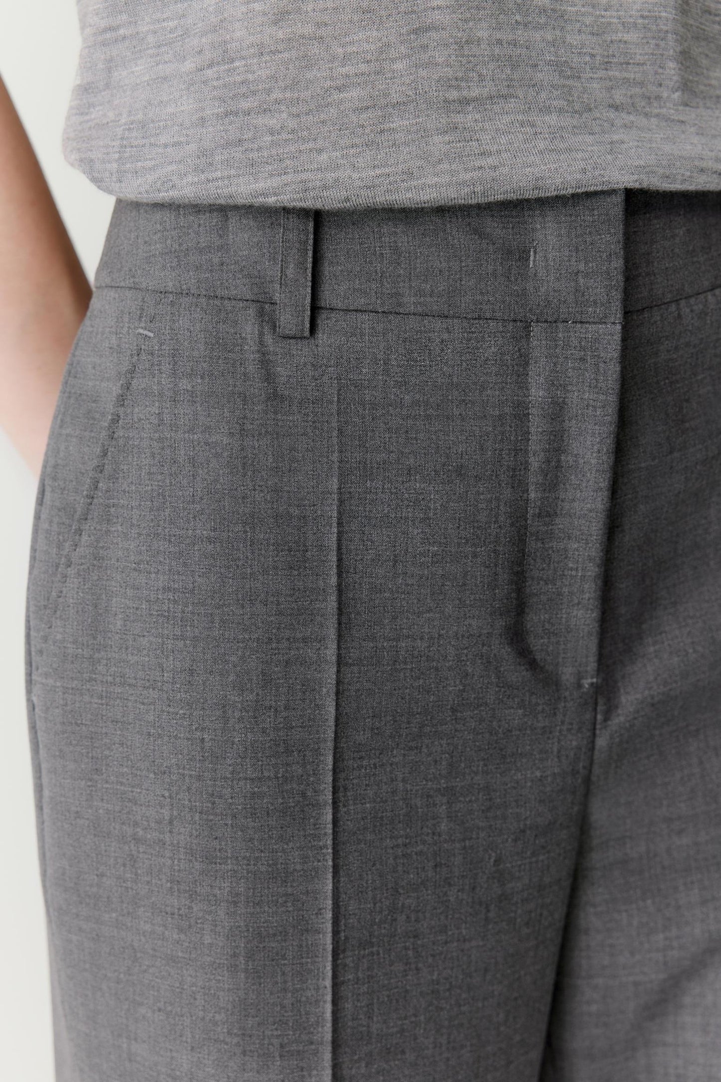 Close-up of the front waistband, revealing the tailored construction, front pleats and clean fastening. The image highlights the smooth texture of the wool fabric and the careful shaping of the upper silhouette.