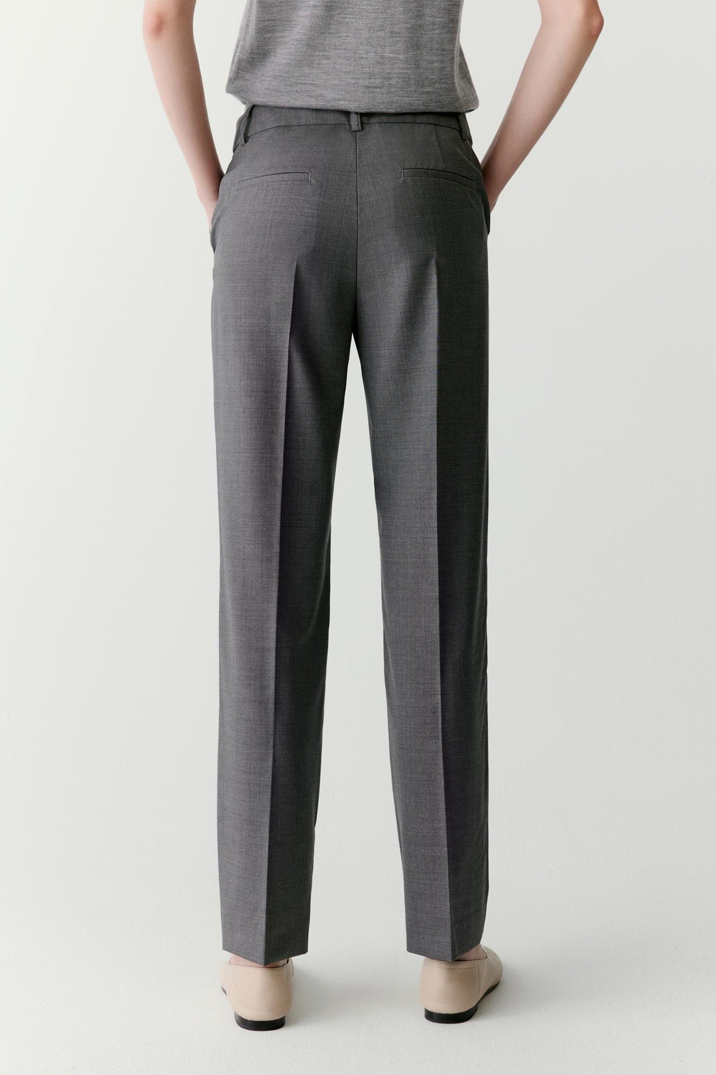 Full-length back view focused on the trousers, showing the tapered cut from hip to ankle, the smooth surface of the worsted wool and the precise construction of the leg. The fabric falls cleanly while maintaining subtle structure.