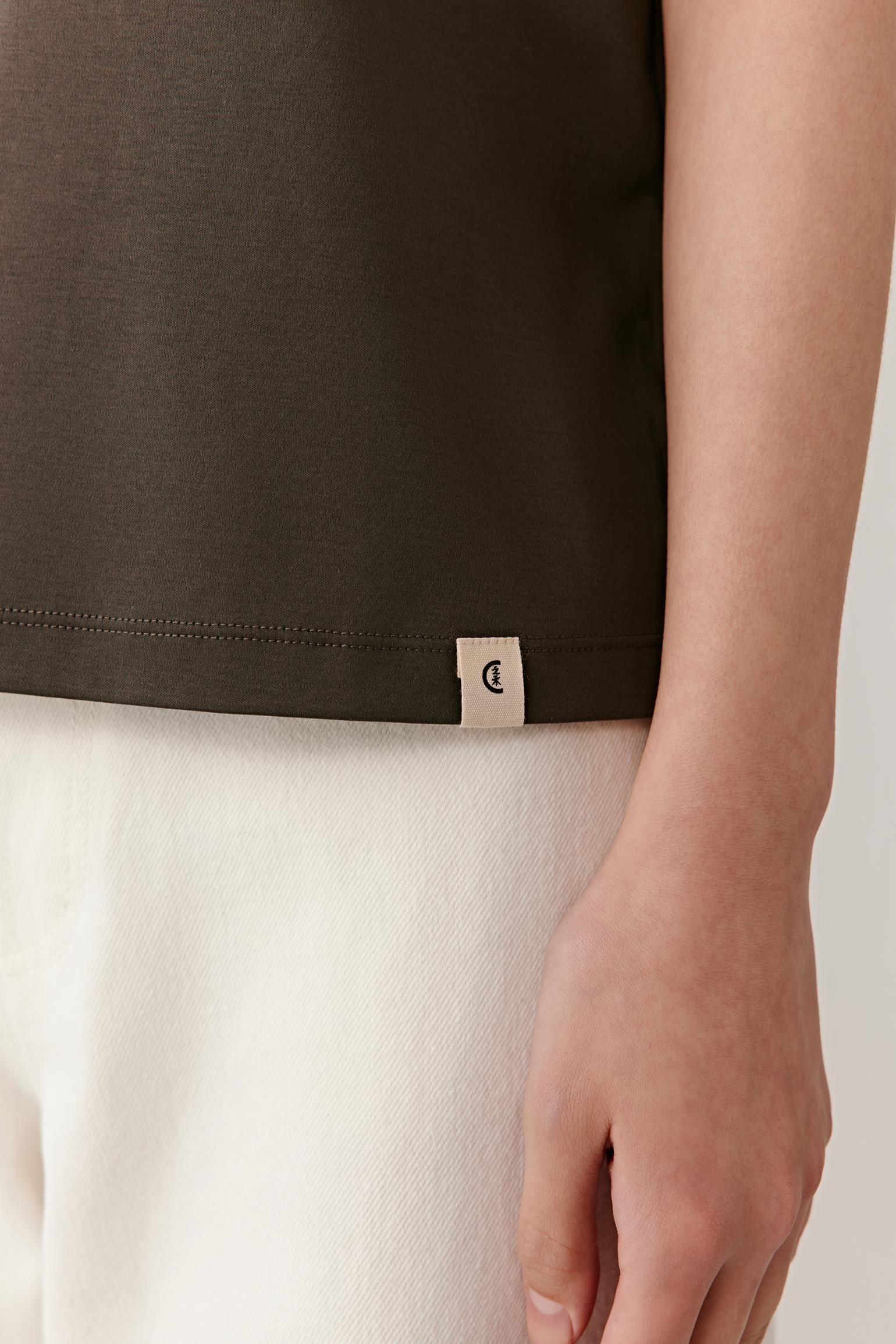 Close-up of the sleeve and side seam area, emphasizing the lightweight jersey construction, smooth surface and clean finishing. The image reveals the soft drape of the fabric, subtle tonal depth and refined simplicity of the cotton jersey.
