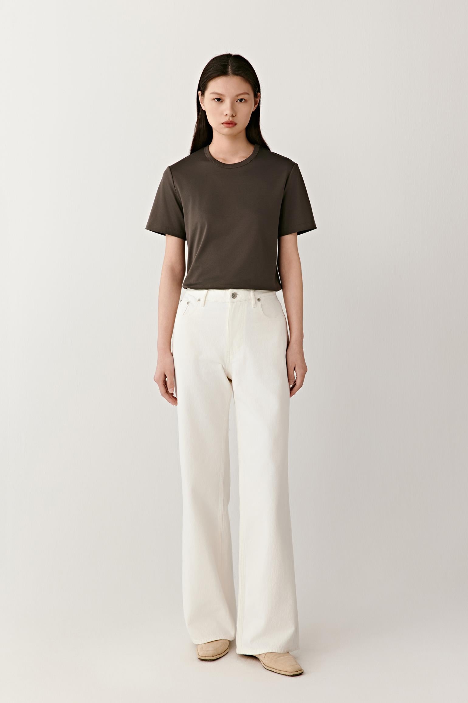Full-length front view showing the T-shirt styled with off-white trousers. The straight cut, round neckline and short sleeves create balanced proportions, while the lightweight jersey construction allows the garment to move naturally and maintain a relaxed silhouette.