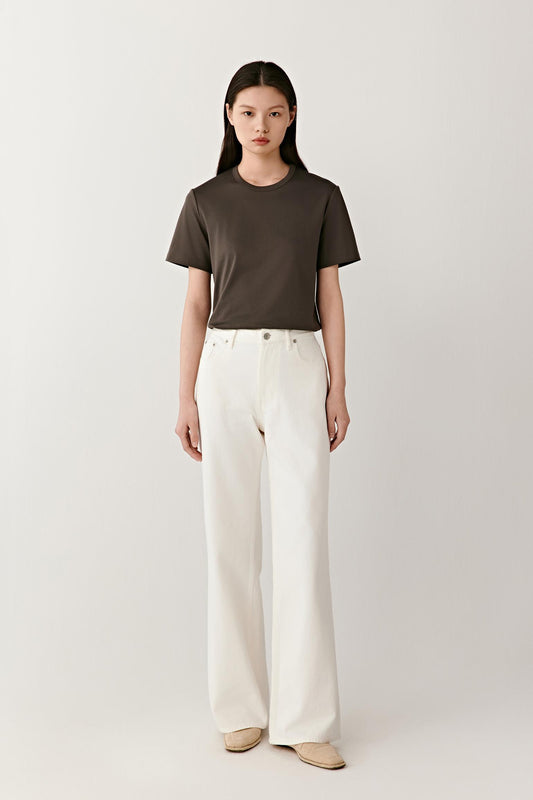 Full-length front view showing the T-shirt styled with off-white trousers. The straight cut, round neckline and short sleeves create balanced proportions, while the lightweight jersey construction allows the garment to move naturally and maintain a relaxed silhouette.