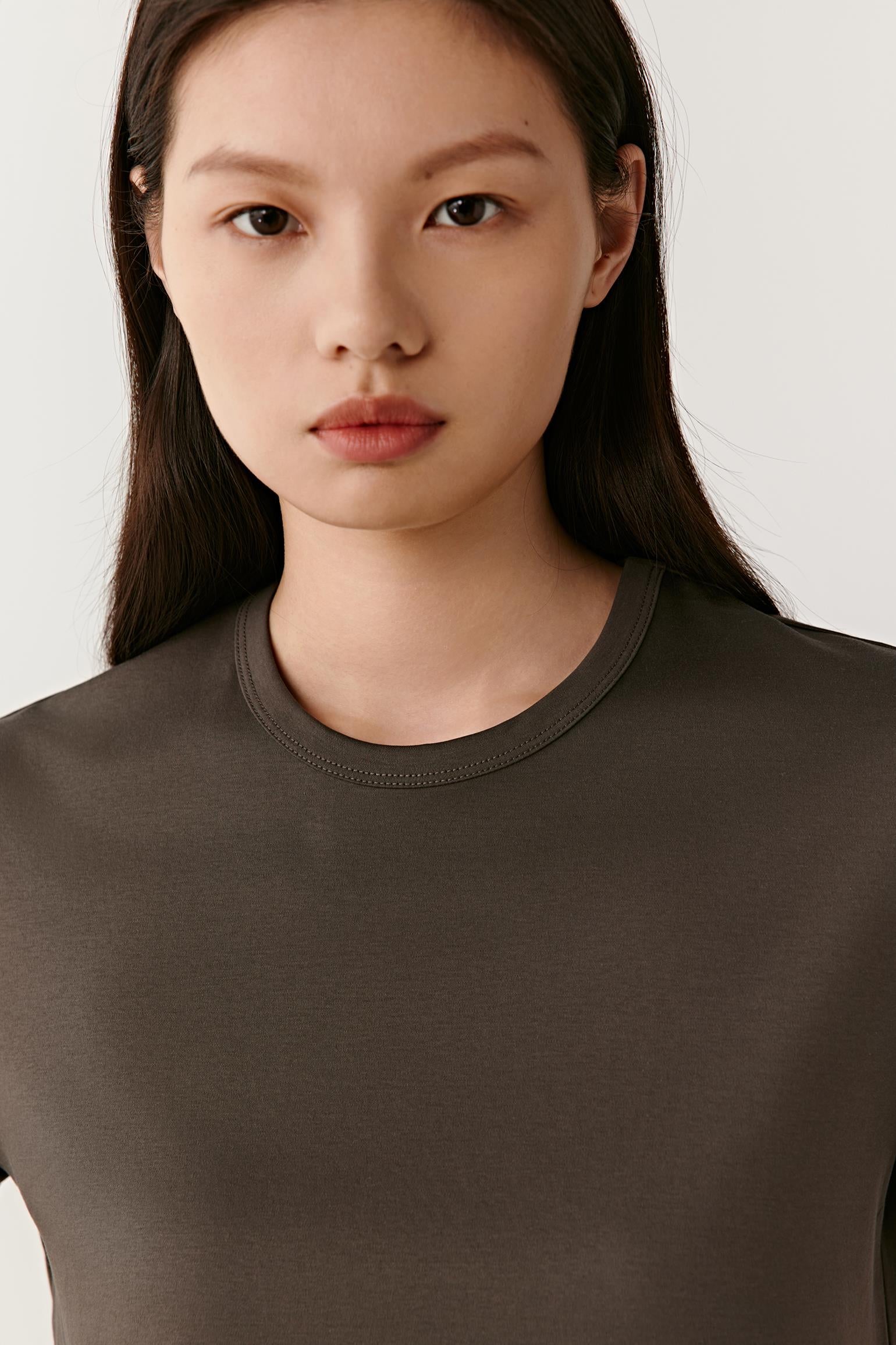 Close-up portrait focusing on the round neckline, shoulder construction and upper body. The image highlights the smooth matte surface, even jersey knit and soft texture, while showcasing the rich dark grey tone and minimal design.