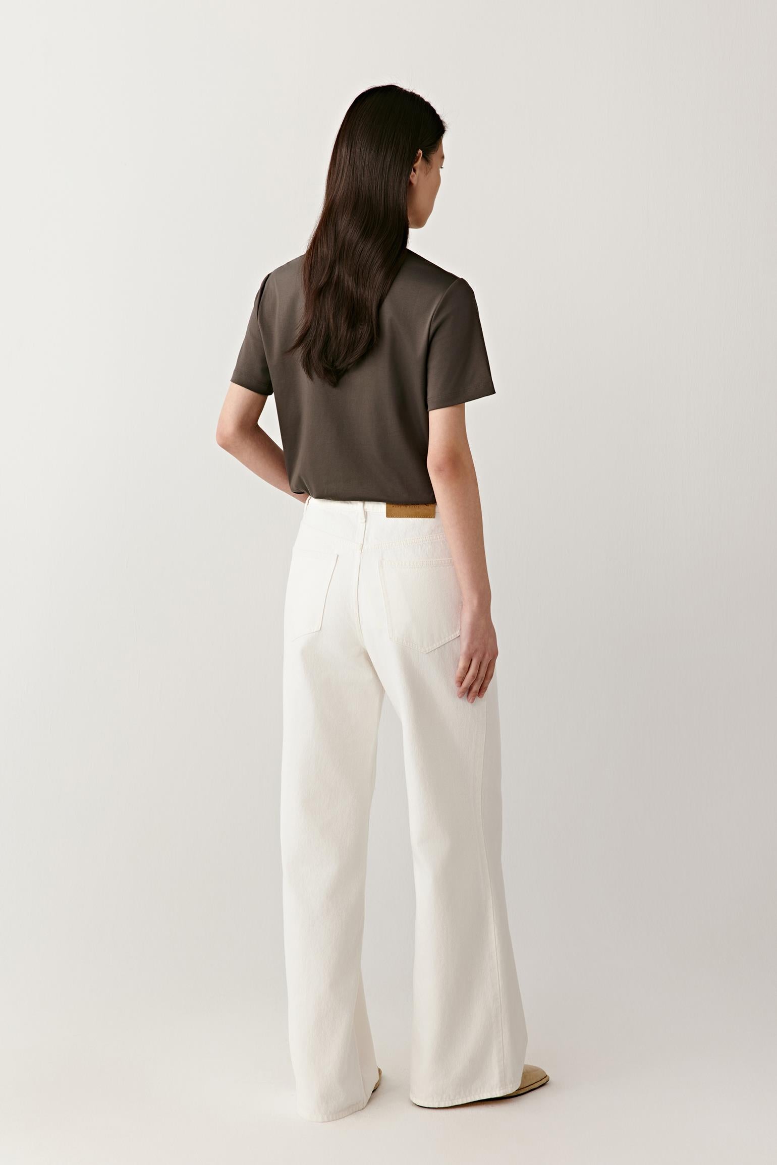 Back view illustrating the fluid drape and soft structure of the cotton jersey. The fabric follows the body without stiffness, creating a clean profile and understated volume through the torso and sleeves.