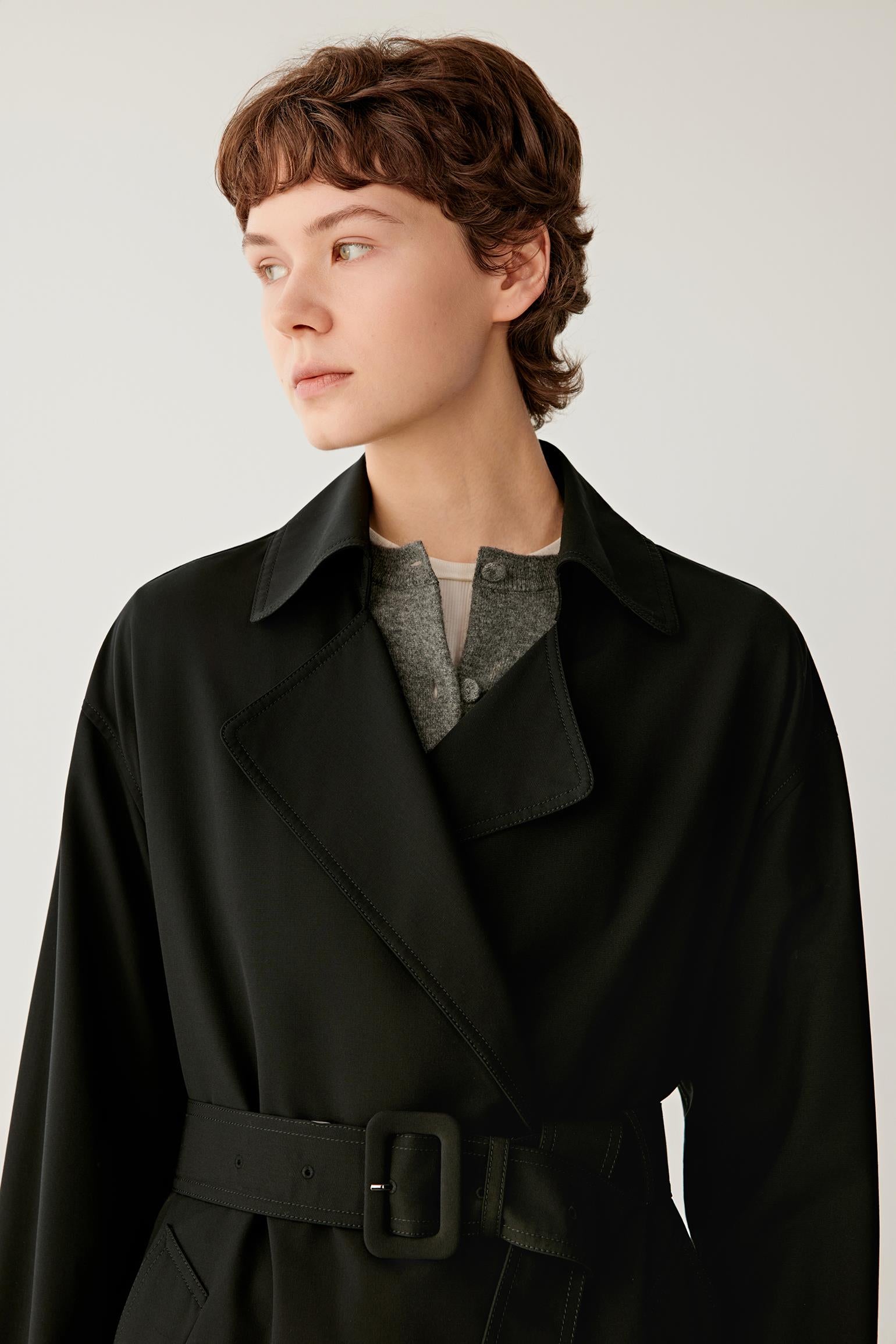 Close-up portrait focusing on the notched lapels, collar construction and upper section of the coat. The image reveals the smooth texture of the fabric, the clean tailoring and the structured neckline that defines the design.