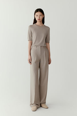 Full-length front view of a model wearing a taupe tee knitted from superfine machine-washable wool. The tee features a straight silhouette with a classic round neckline and short sleeves that fall naturally along the upper arm. The lightweight knit creates a soft and fluid drape across the torso.