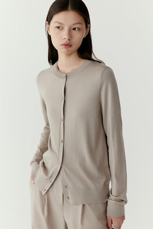 Front view of a model wearing a taupe wool cardigan with a clean straight silhouette. The cardigan features a round neckline and a central button placket with tonal buttons. The long sleeves extend to the wrists and the fine wool knit creates a smooth and lightweight texture.