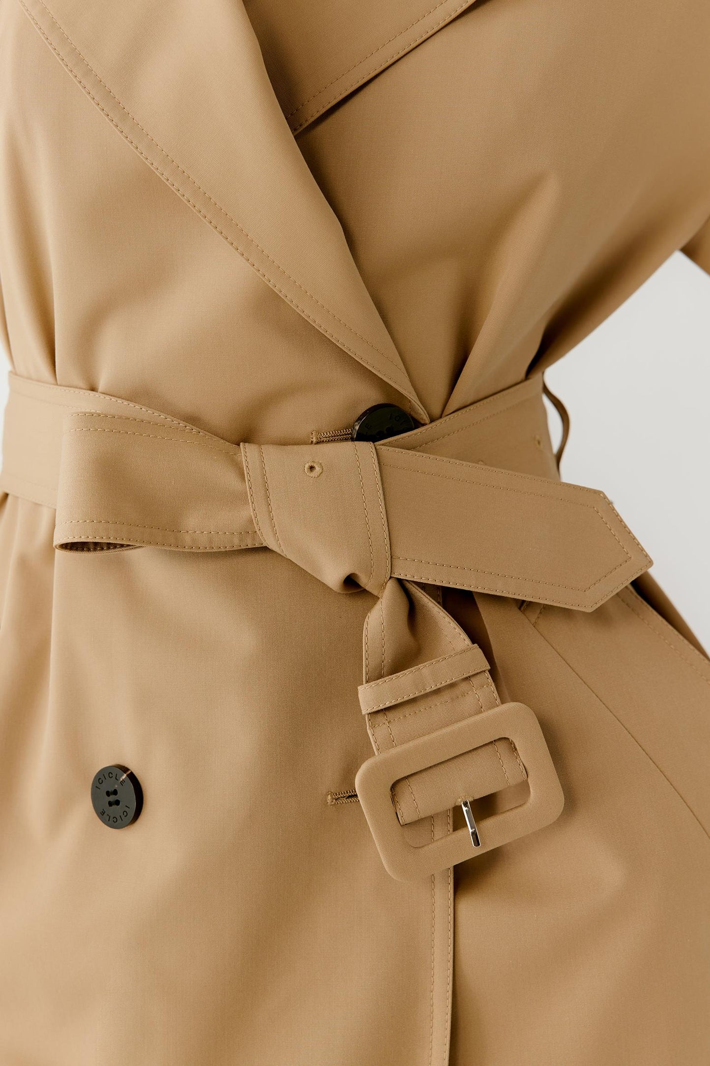 Close-up view of the waist area highlighting the self-fabric belt, belt loops and double-breasted button fastening. The image showcases the structured construction, precise finishing and the way the belt defines the silhouette while maintaining fluidity.