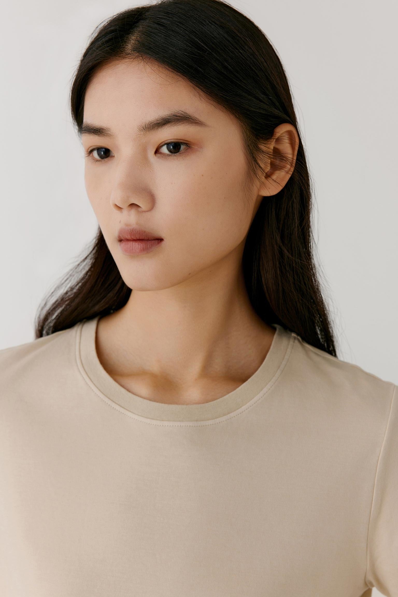 Close-up portrait focusing on the round neckline, shoulder construction and upper body. The image reveals the smooth texture of the cotton jersey, the soft finish of the fabric and the clean, minimal lines of the design.