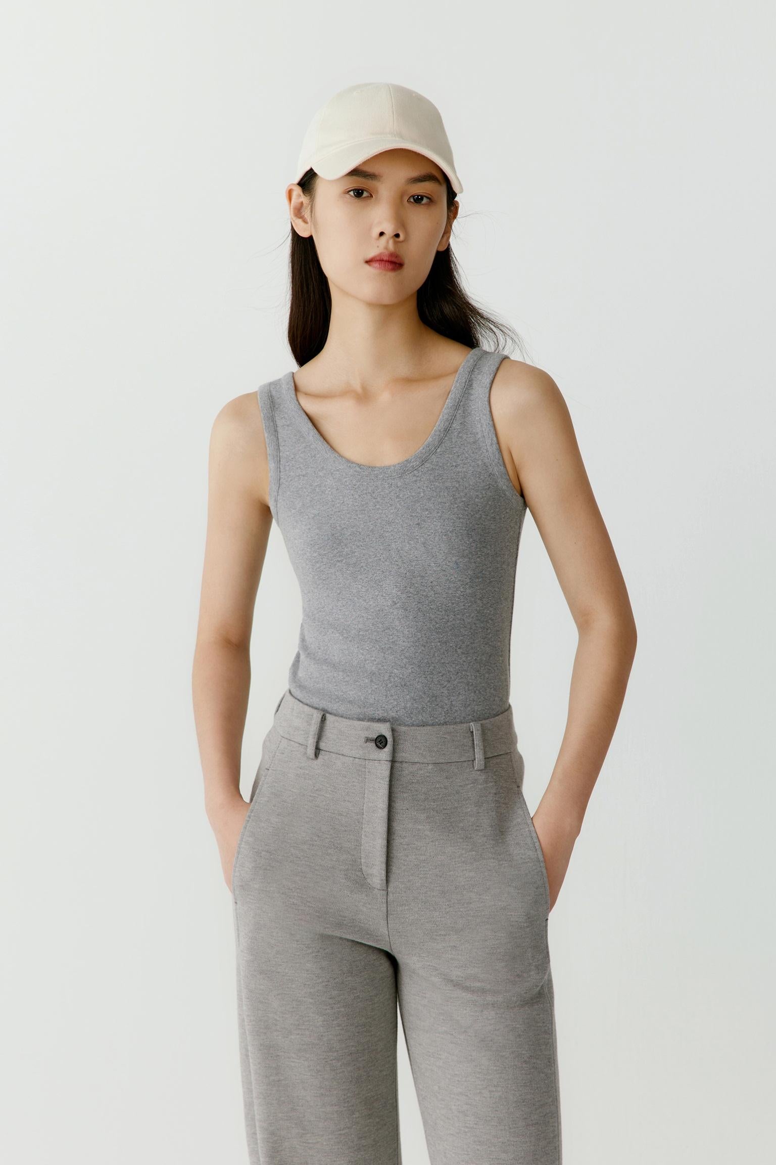 Front view of a woman wearing a grey rib jersey tank top, highlighting the close-fitting silhouette, soft ribbed texture and clean construction. The sleeveless cut and rounded neckline create a simple and balanced appearance.