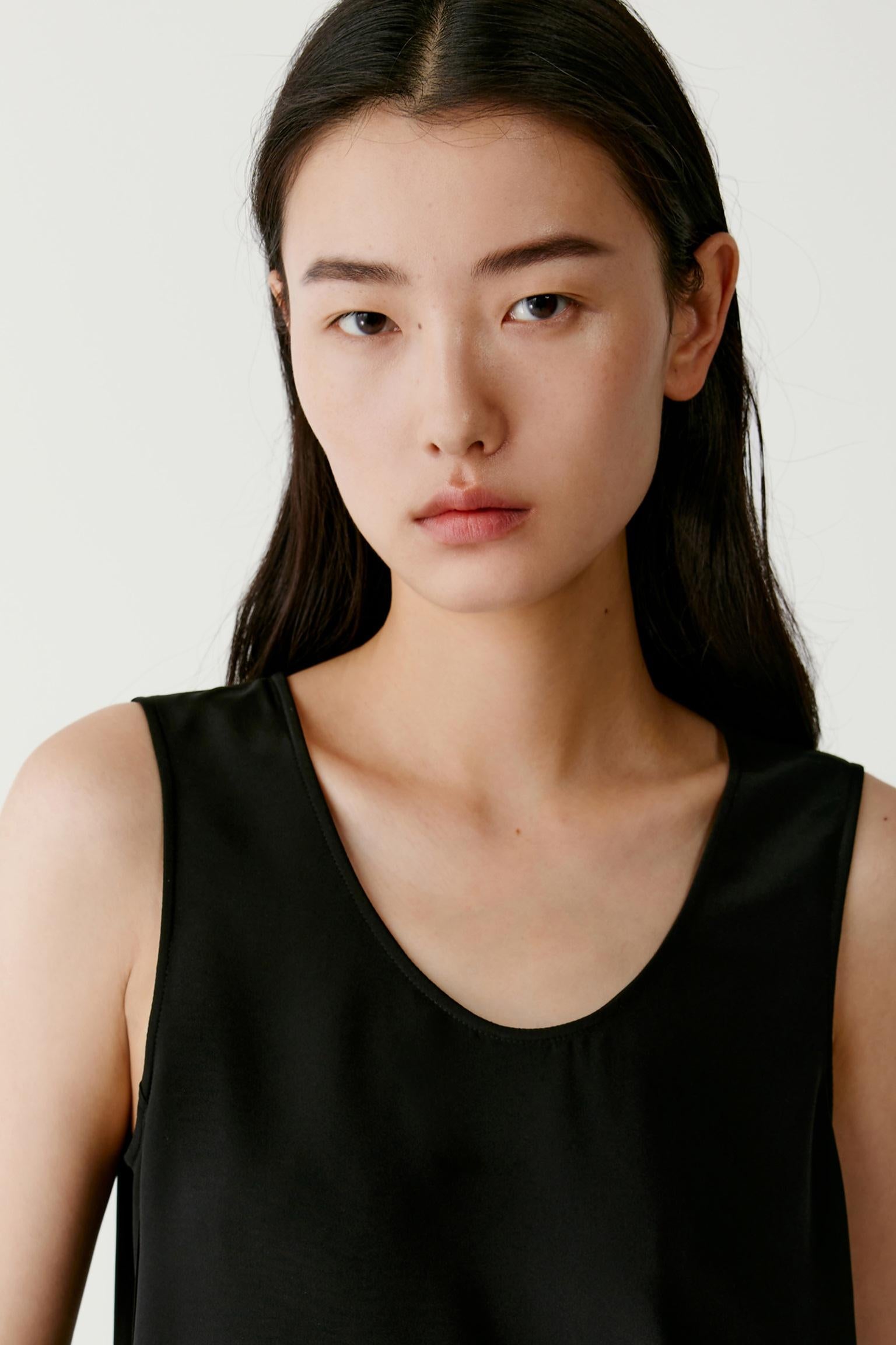 Close-up portrait focusing on the round neckline, shoulder line and upper section of the garment. The image reveals the smooth texture, soft finish and subtle lustre characteristic of silk crêpe de Chine while emphasizing the minimalist construction and clean lines.
