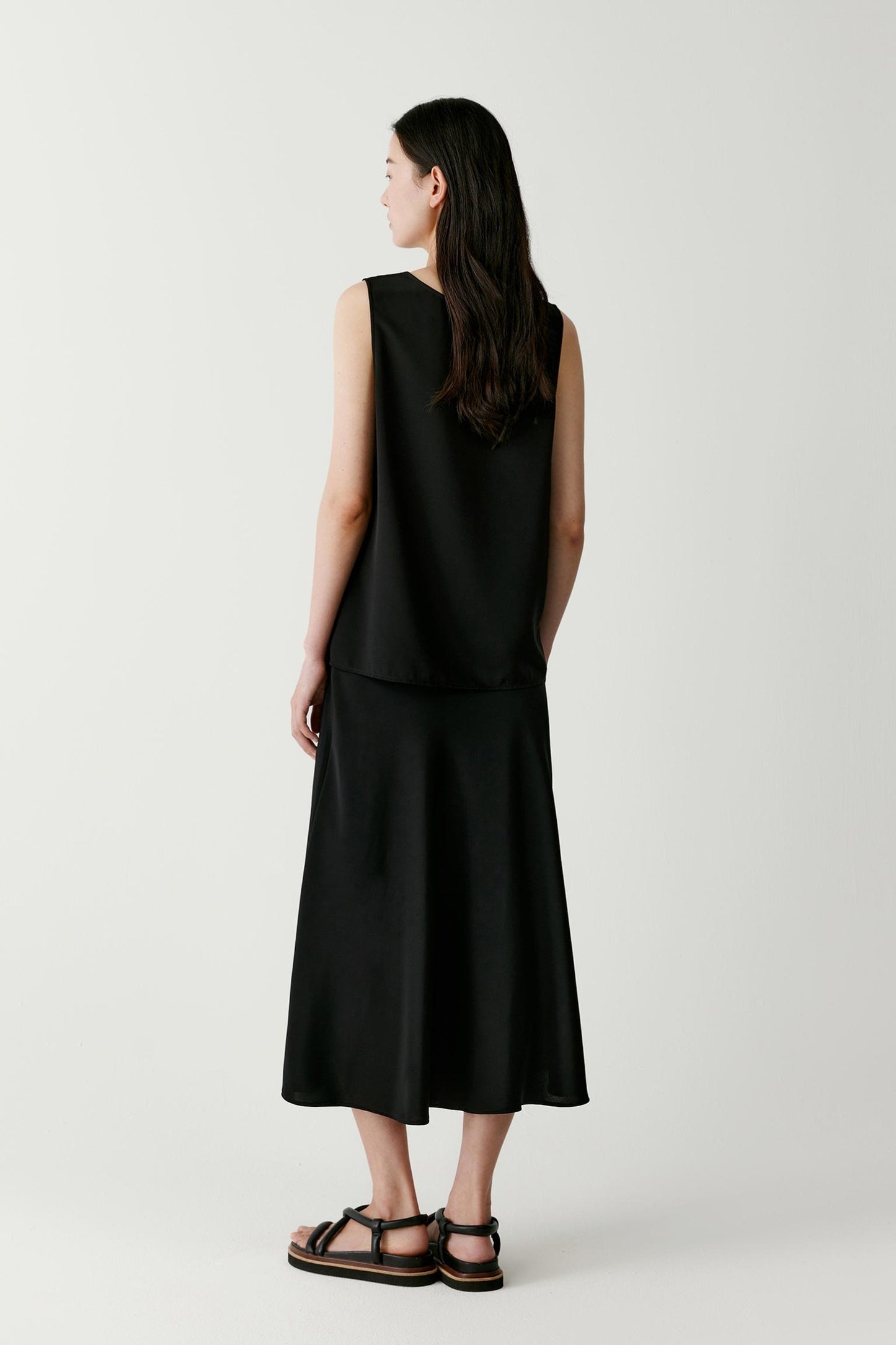 Side view highlighting the fluid fall of the fabric from shoulder to hem. The image showcases the sleeveless construction, clean side line and lightweight structure of the silk fabric, revealing the ease and movement of the garment.