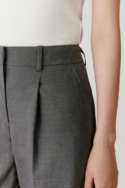 Close-up detail highlighting the waistband construction, belt loops and front pleats that shape the upper part of the trousers.