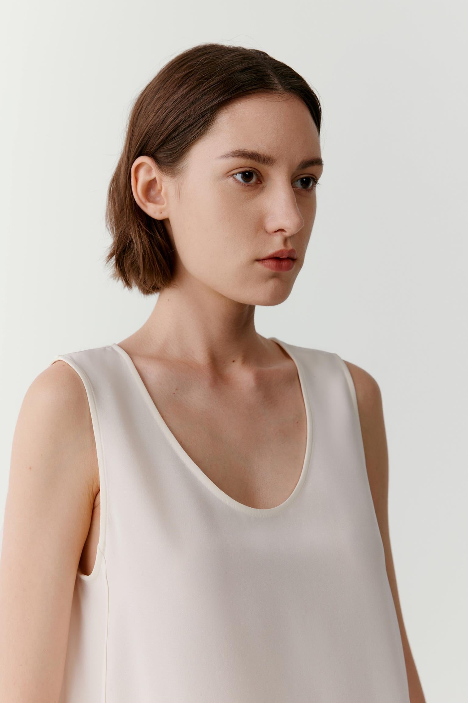 Close-up portrait focusing on the round neckline, shoulder line and upper section of the garment. The image reveals the smooth texture, soft finish and subtle lustre characteristic of silk crêpe de Chine while emphasizing the minimalist construction.