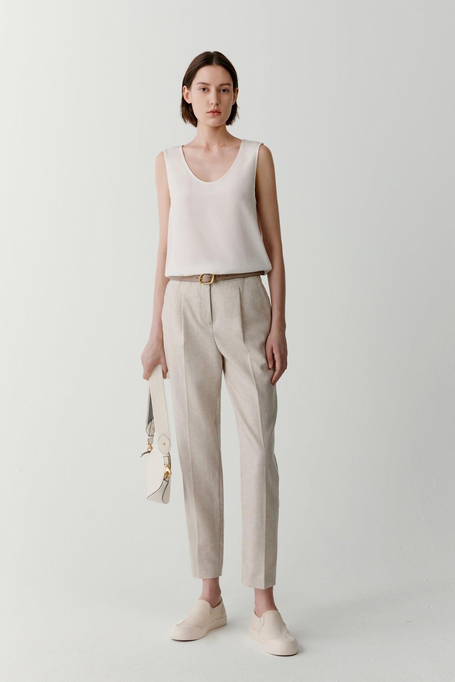Front view of a woman wearing a sleeveless top in white silk crêpe de Chine. The image highlights the fluid drape, smooth surface and soft hand of the fabric. The relaxed silhouette falls naturally from the shoulders, while the round neckline and sleeveless construction create a clean and understated appearance.