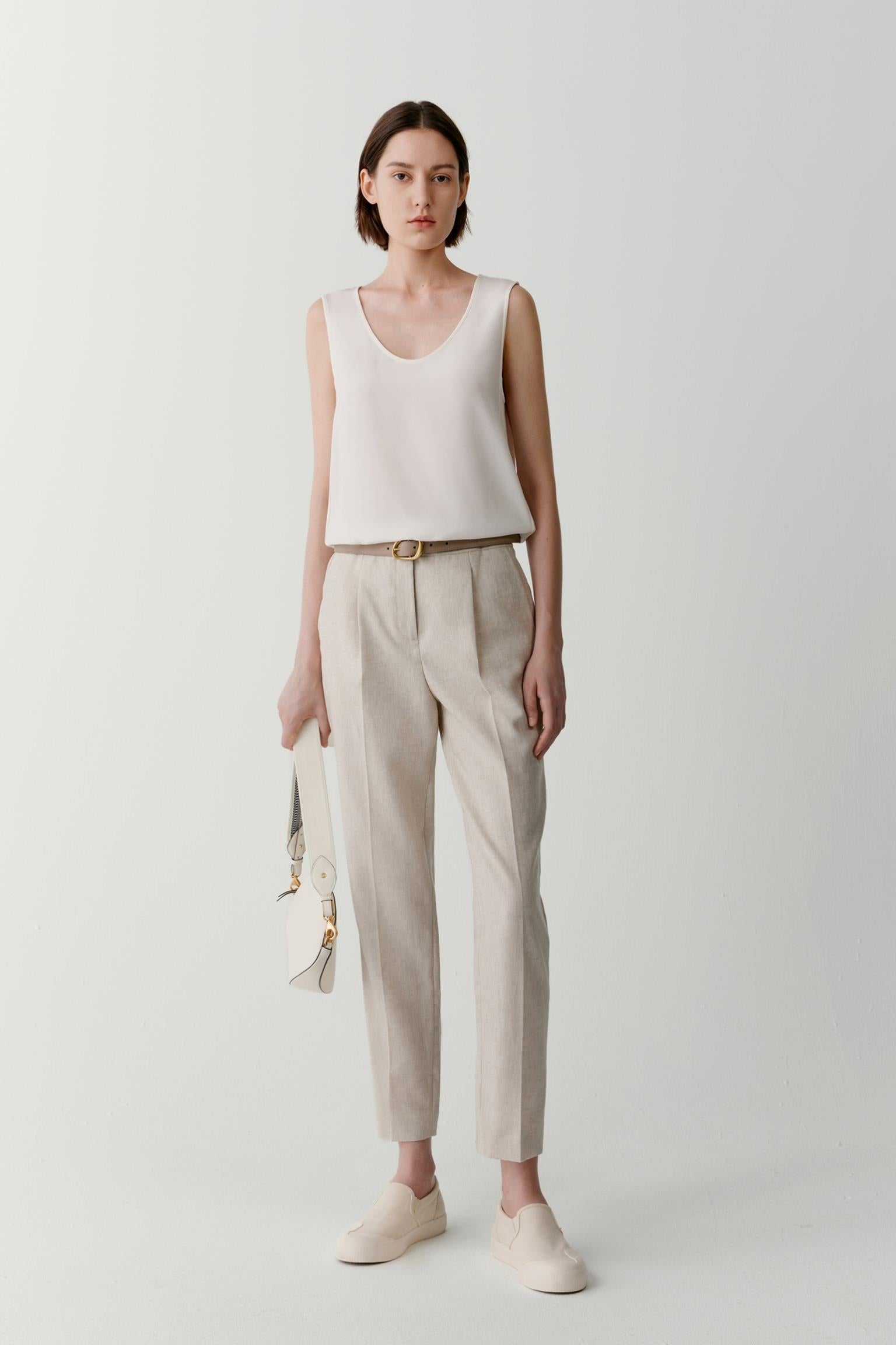 Front view of a woman wearing a sleeveless top in white silk crêpe de Chine. The image highlights the fluid drape, smooth surface and soft hand of the fabric. The relaxed silhouette falls naturally from the shoulders, while the round neckline and sleeveless construction create a clean and understated appearance.