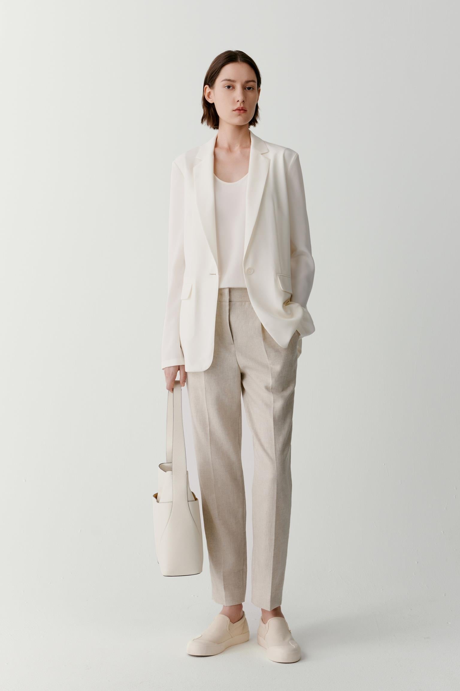 Front view of a woman wearing a blazer in white silk crêpe de Chine. The image highlights the fluid drape of the fabric, the softly structured silhouette and the lightweight construction. Notched lapels, a single-button fastening and long sleeves create a tailored appearance, while the smooth surface of the silk contributes to a refined finish.