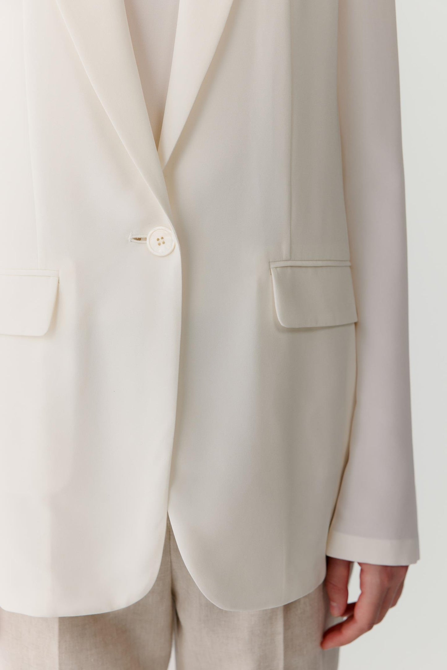 Close-up view of the lower front section of the blazer highlighting the flap pocket, sleeve construction and clean finishing. The image showcases the smooth surface of the silk crêpe de Chine, the lightweight structure of the fabric and the precise tailoring details that define the garment.
