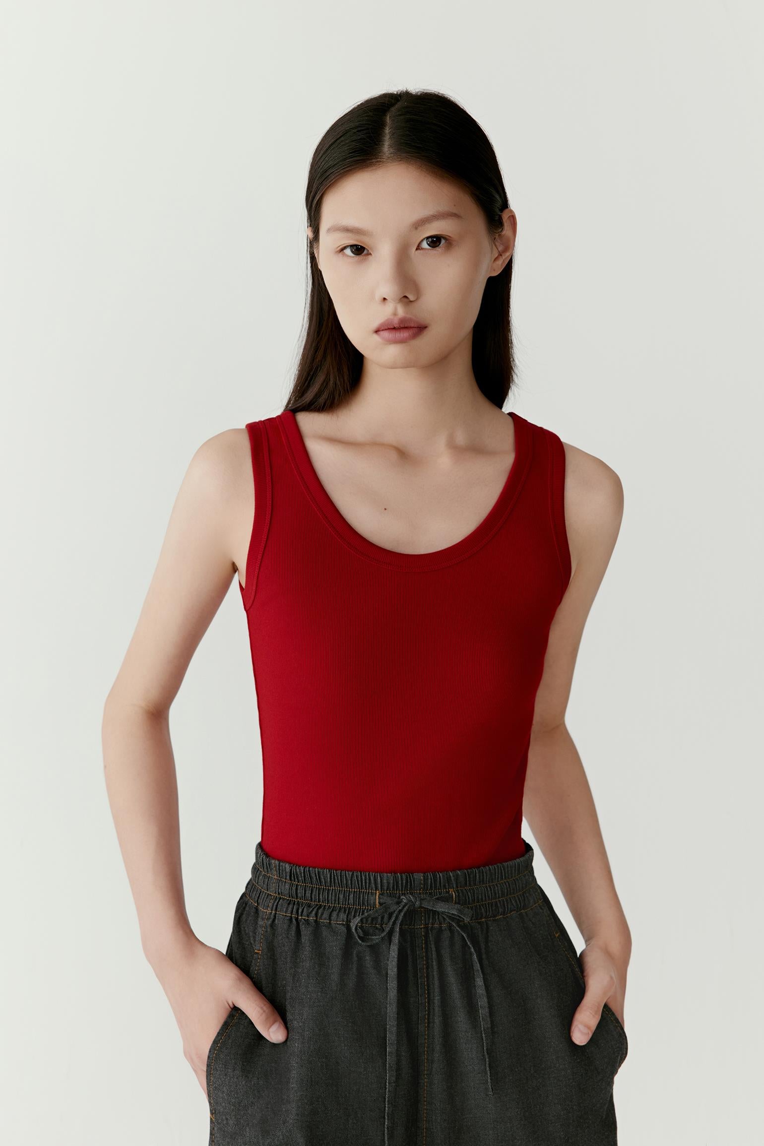 Front view of a woman wearing a deep red tank top in cotton rib jersey, highlighting the finely textured ribbed surface, close-fitting silhouette and soft hand. The rich colour emphasizes the vertical rib structure, while the sleeveless construction creates a clean and balanced appearance.