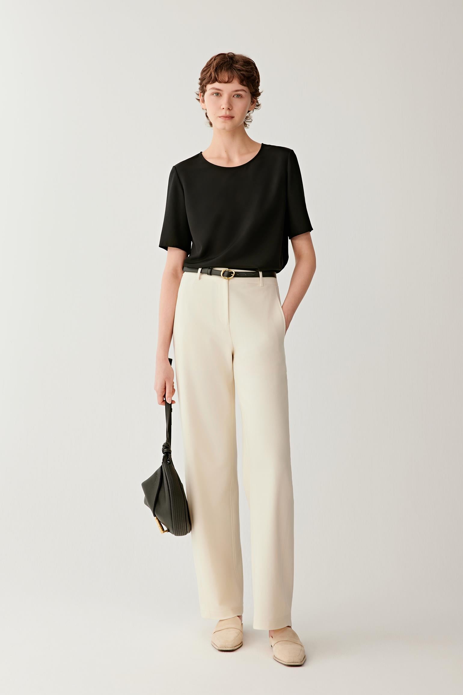 Front view of a woman wearing a shirt in deep black silk crêpe de Chine. The image highlights the fluid drape, smooth surface and soft hand of the fabric. The relaxed silhouette falls naturally from the shoulders, while the wide round neckline and short sleeves create a clean, understated appearance.