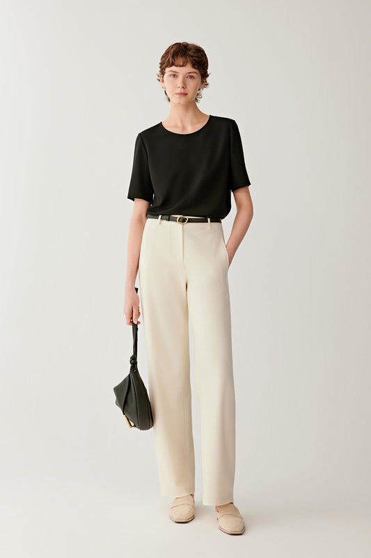Front view of a woman wearing a shirt in deep black silk crêpe de Chine. The image highlights the fluid drape, smooth surface and soft hand of the fabric. The relaxed silhouette falls naturally from the shoulders, while the wide round neckline and short sleeves create a clean, understated appearance.