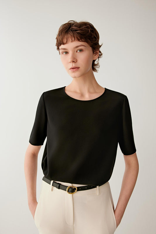 Three-quarter view showing the fluid movement of the silk crêpe de Chine and the relaxed proportions of the garment. The image emphasizes the lightweight construction, soft drape and minimalist silhouette defined by clean lines and a smooth surface.