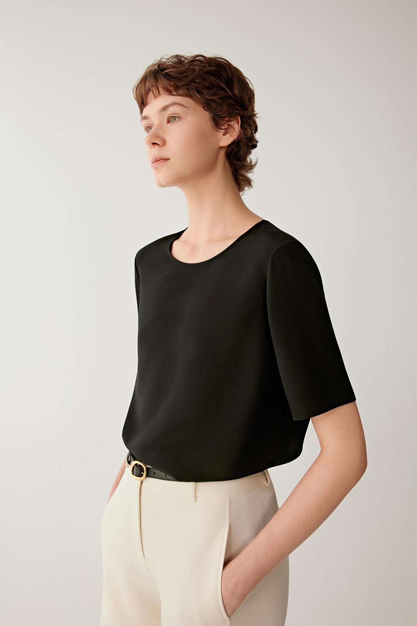 Side view highlighting the fluid fall of the fabric through the body and sleeves. The image showcases the relaxed cut, subtle volume and soft movement created by the lightweight silk construction.