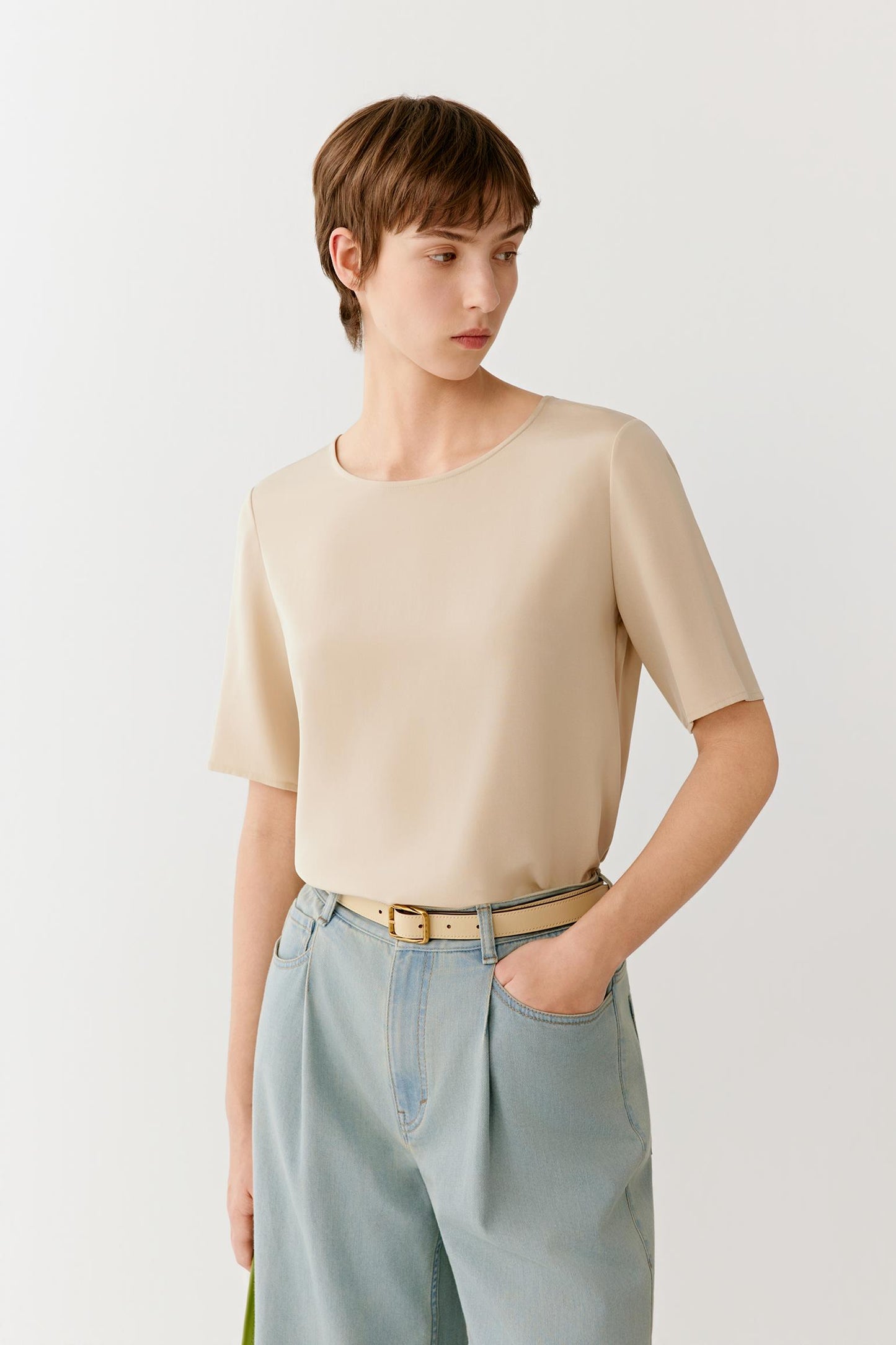 Three-quarter view highlighting the relaxed fit and fluid movement of the garment. The image showcases the soft structure of the short sleeves, the smooth surface of the silk fabric and the clean lines that define the silhouette.