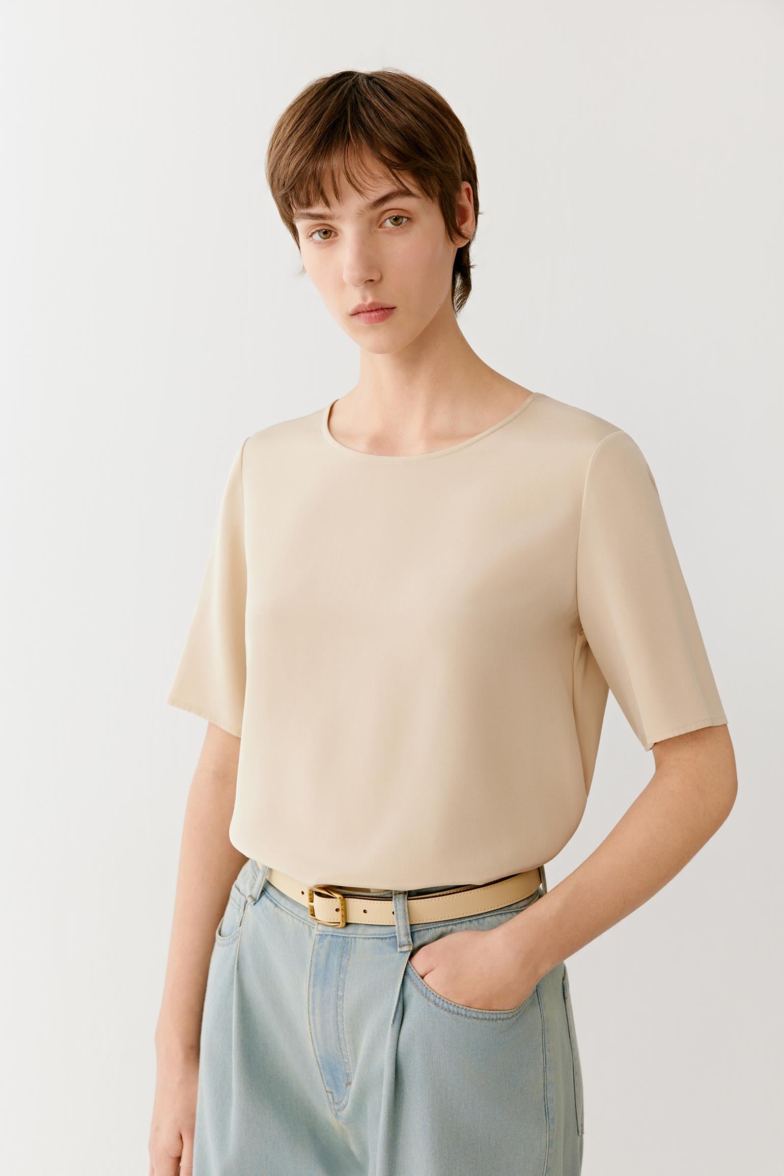 Close-up view focusing on the neckline, shoulder line and upper section of the garment. The image reveals the smooth texture, subtle lustre and refined finish of the silk crêpe de Chine while emphasizing the minimalist construction and fluid drape.