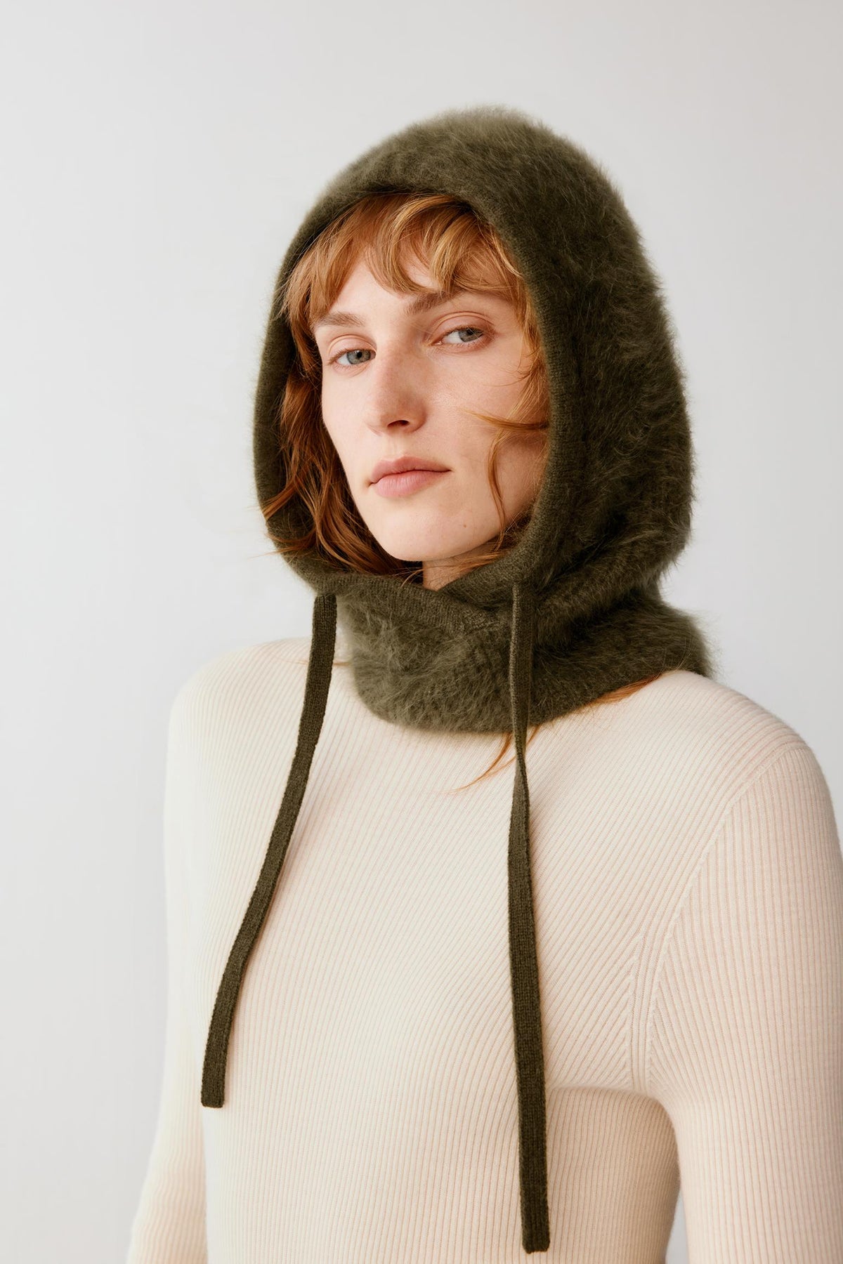 Front view of a woman wearing the dark green brushed cashmere balaclava, highlighting the hood and long front panels.