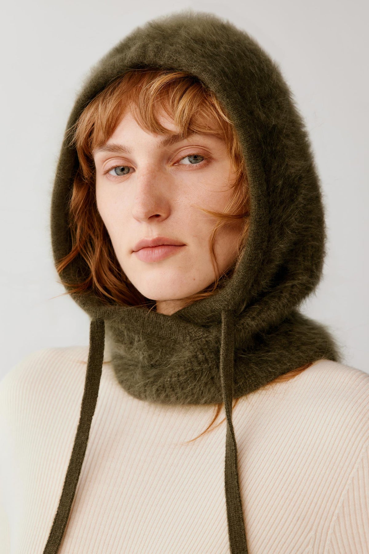 Side view of a woman wearing the dark green brushed cashmere balaclava, highlighting the hooded construction and long front panels.