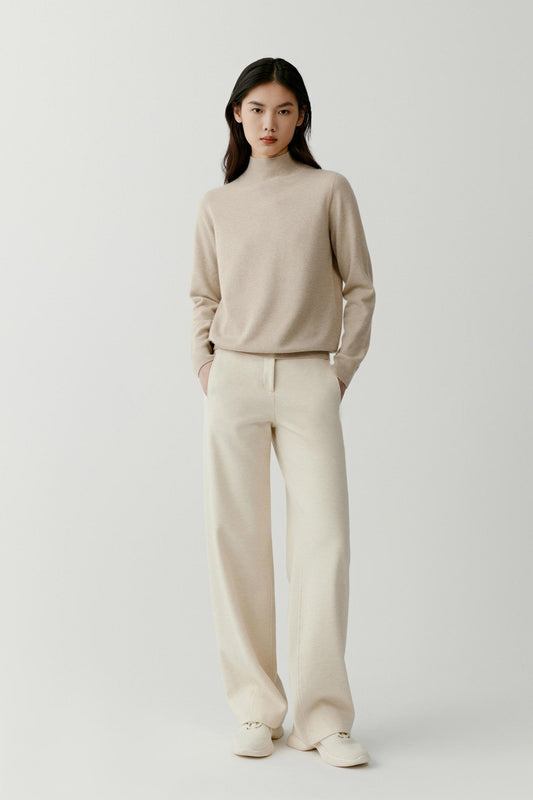 Front view of a woman wearing a beige cashmere pullover, showing the mock neck, dropped shoulders and relaxed silhouette.