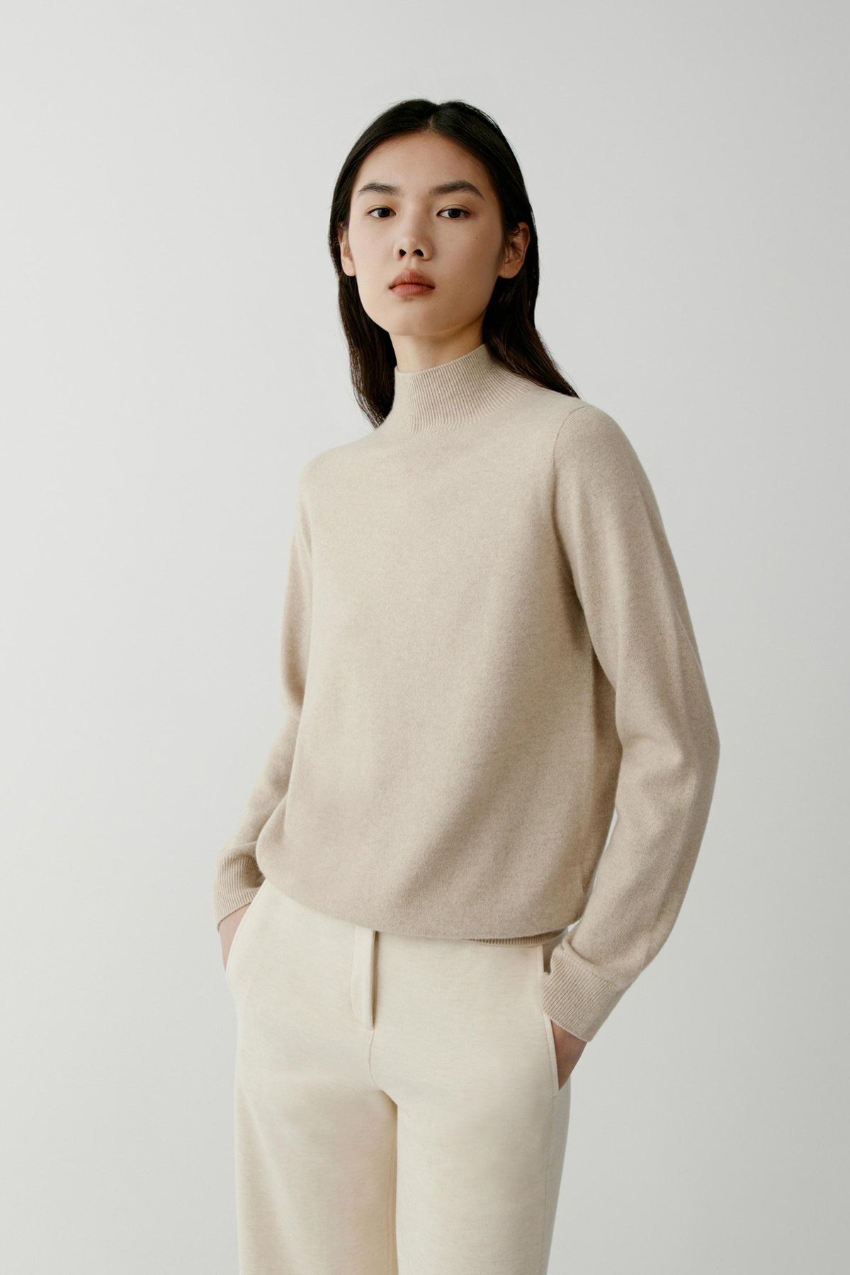 Three-quarter view highlighting the mock neck, long sleeves and fine-knit construction of the beige cashmere pullover.