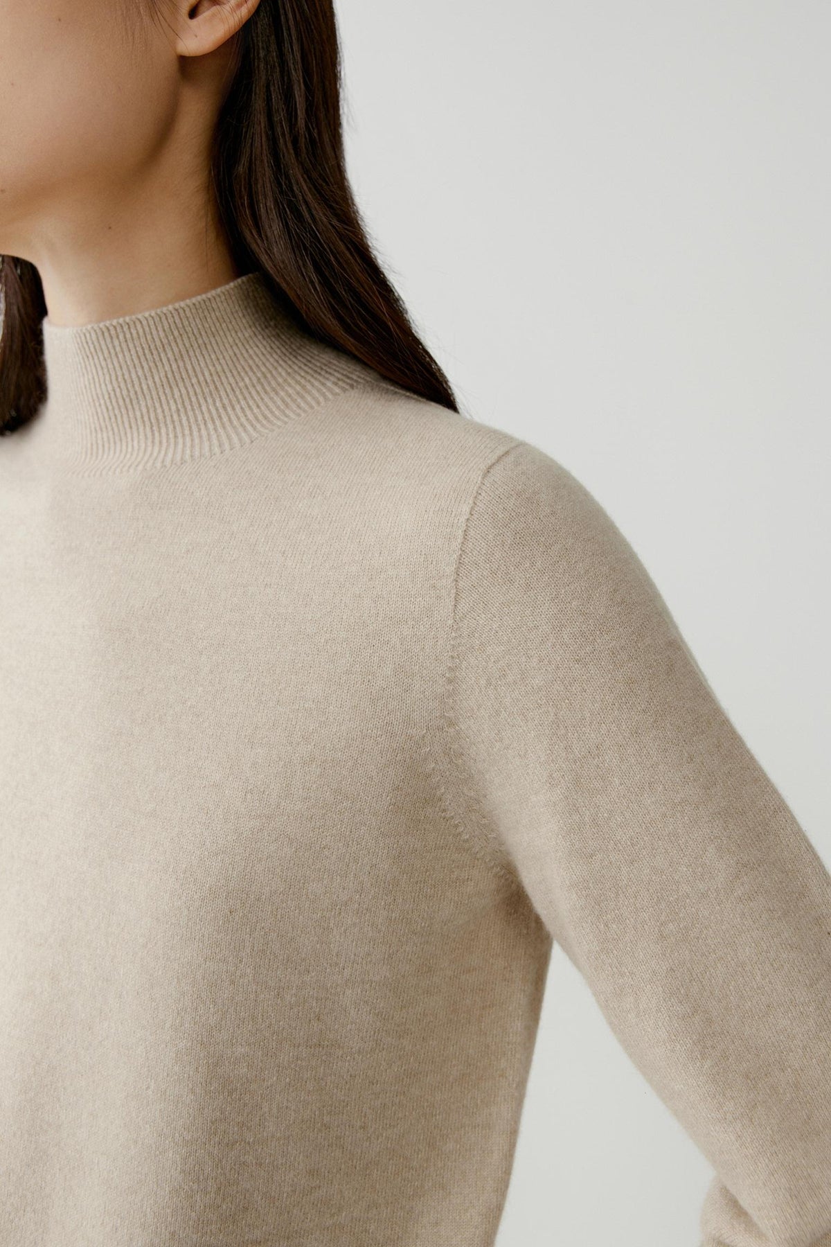 Close-up highlighting the dropped shoulder, long sleeve and smooth beige cashmere surface.
