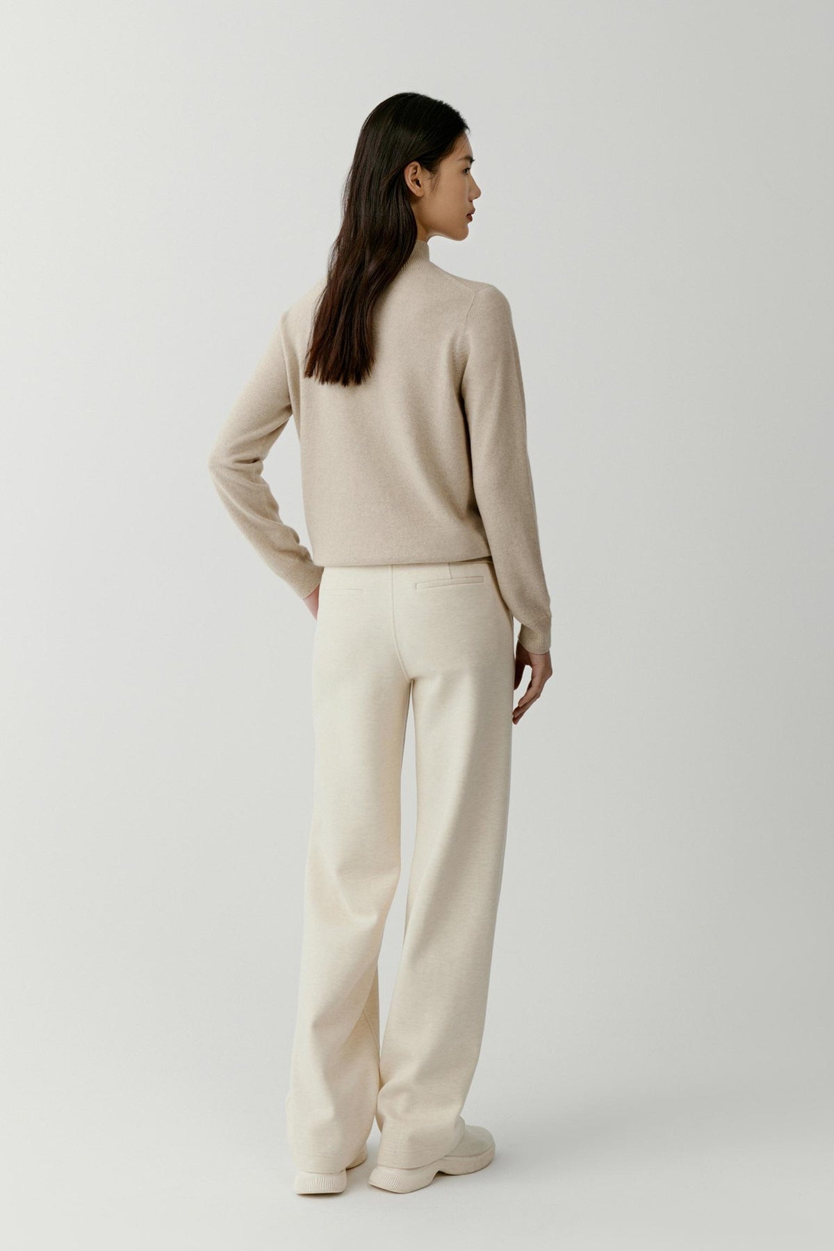 Side view of a woman wearing the beige cashmere pullover, showing the relaxed silhouette and clean knit construction.