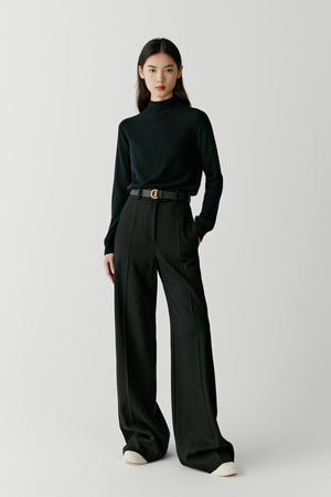 Front view of a woman wearing a deep black cashmere pullover, showing the mock neck, dropped shoulders and relaxed silhouette.