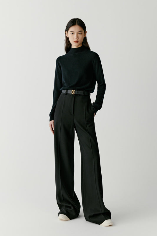 Front view of a woman wearing a deep black cashmere pullover, showing the mock neck, dropped shoulders and relaxed silhouette.