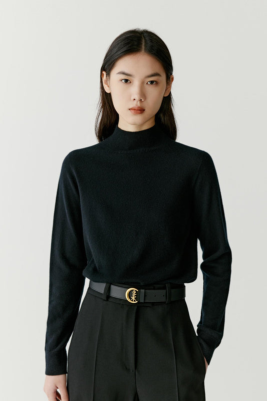 A model wearing a black long-sleeve mock neck knit sweater tucked into black trousers with a black belt featuring a gold-tone double-C buckle.