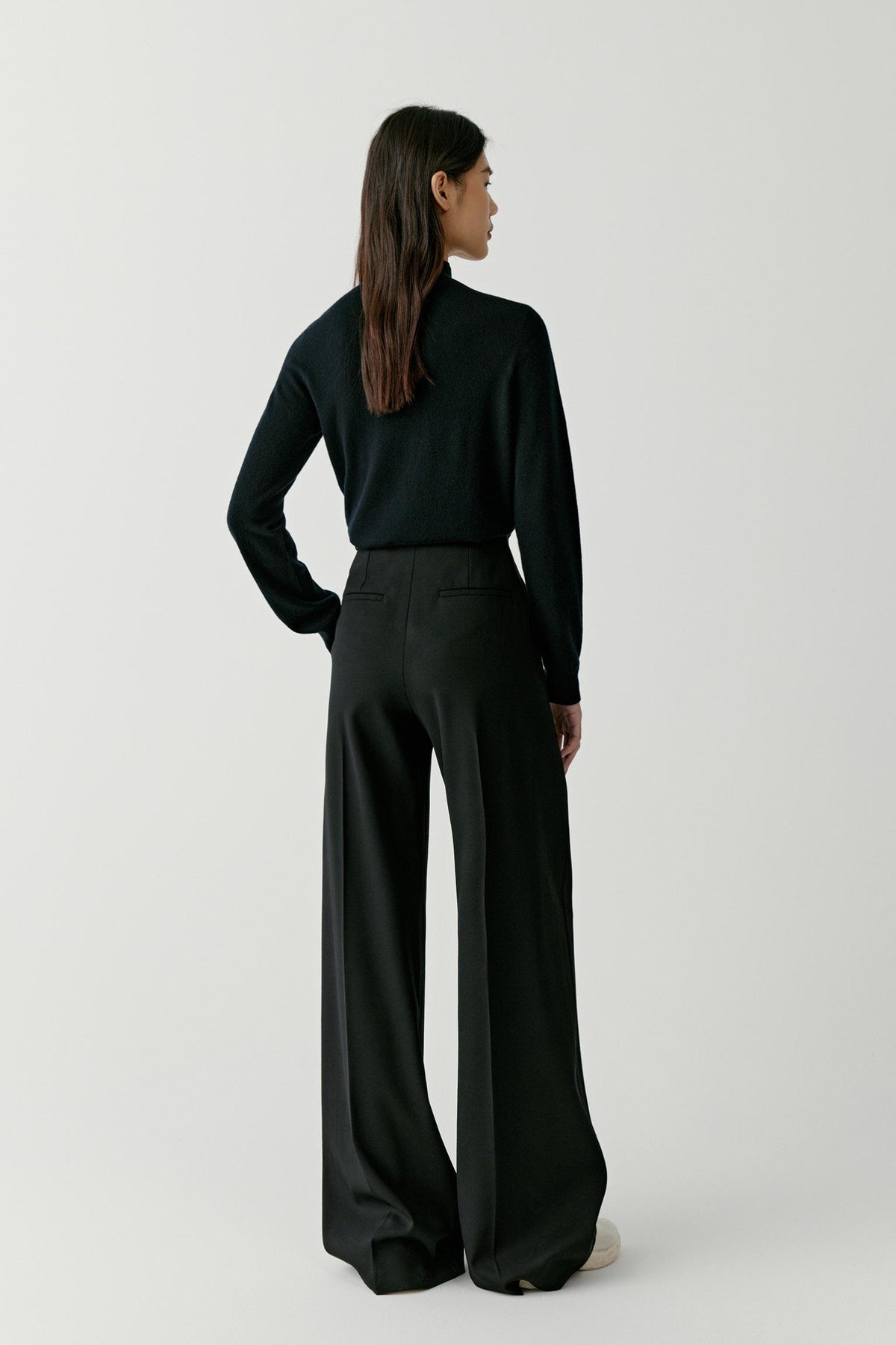 Full-length view of a woman wearing a deep black cashmere pullover, showing the relaxed fit and clean silhouette.