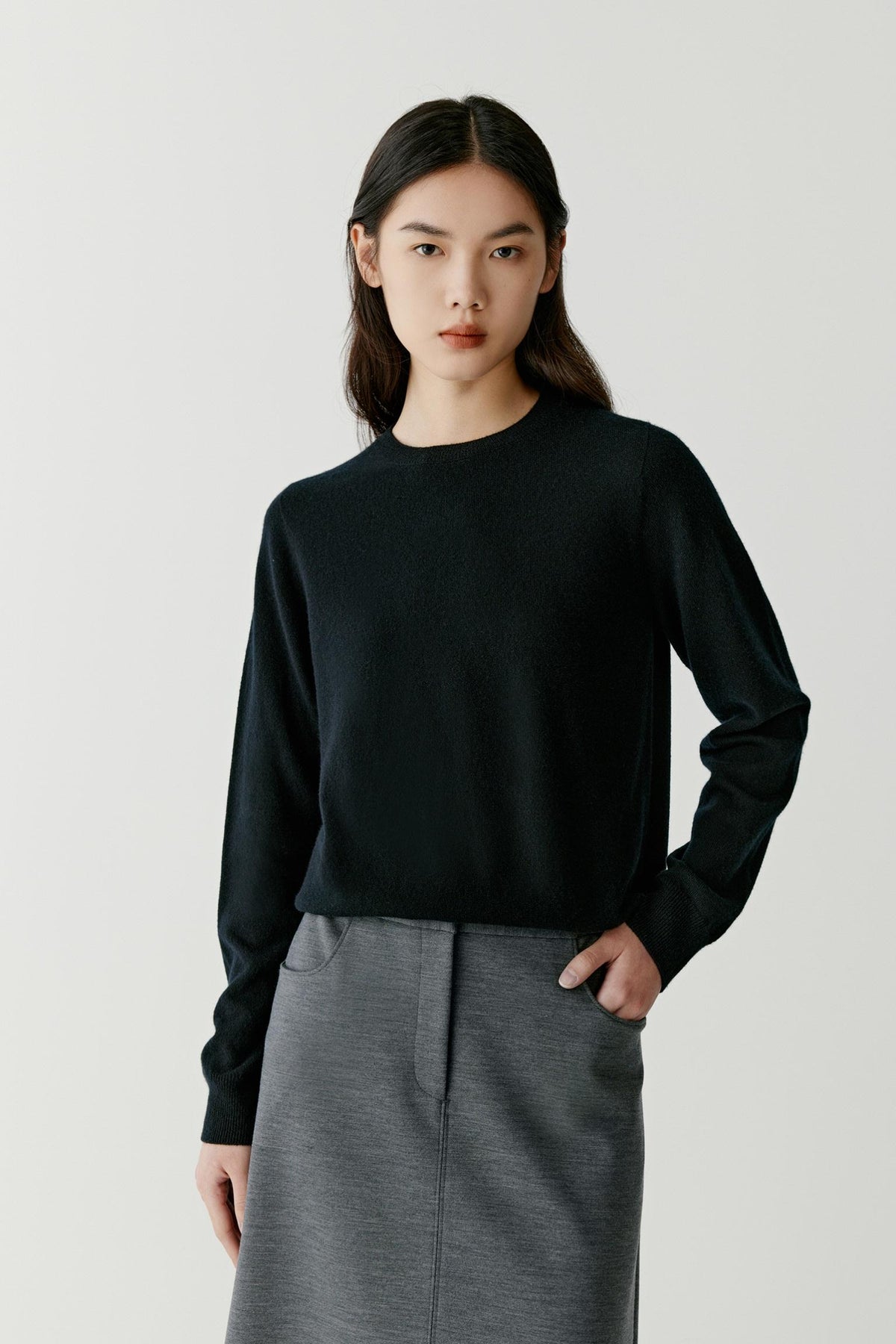 Front view of a woman wearing a deep black cashmere pullover, showing the crew neckline, long sleeves and relaxed silhouette.