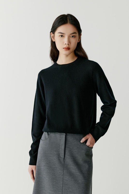 Front view of a woman wearing a deep black cashmere pullover, showing the crew neckline, long sleeves and relaxed silhouette.